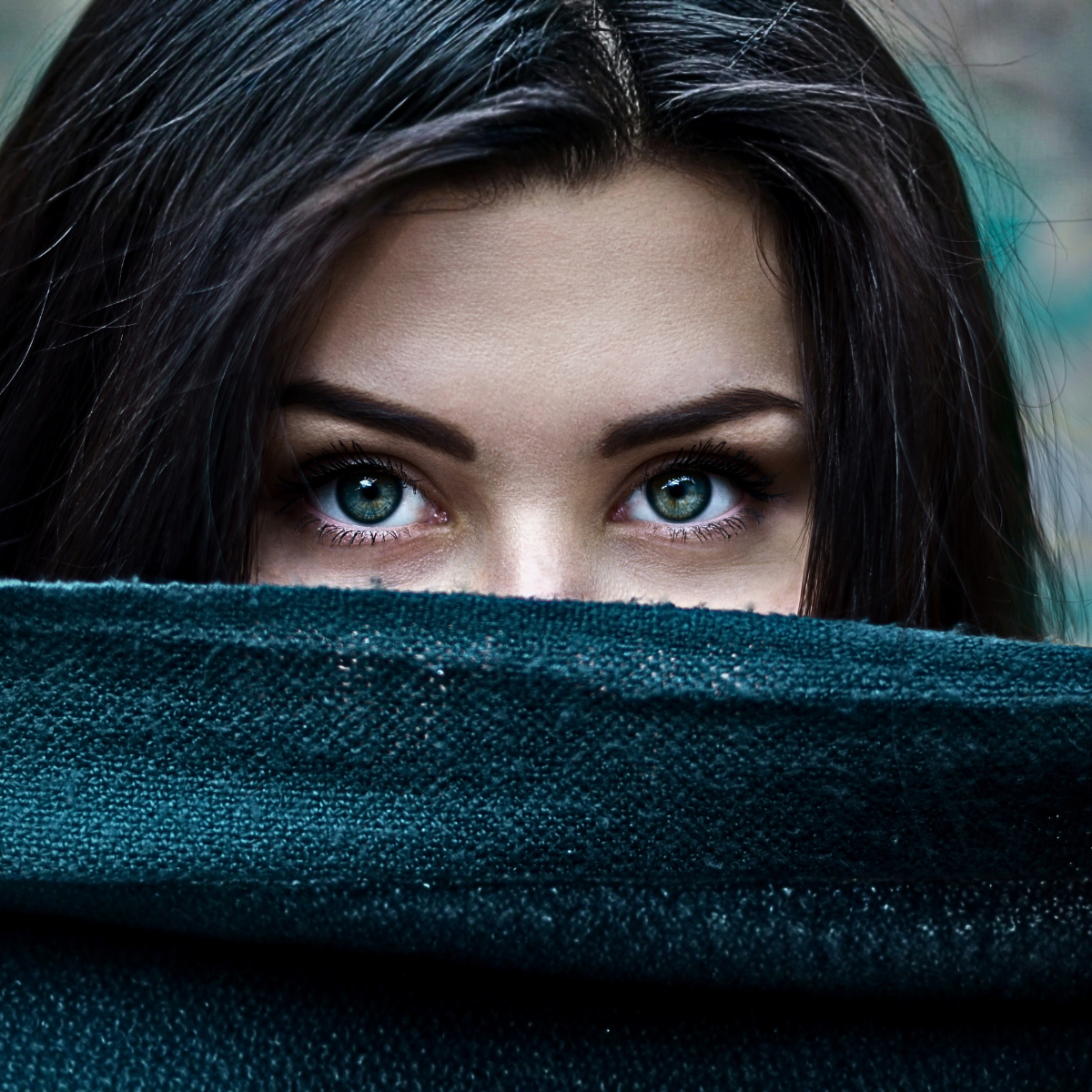 A beautiful Model with Black Hair is looking into the camera with her blue eyes, holding a dark teal blanket that she is peeking over ©2025 Kandilynns.com